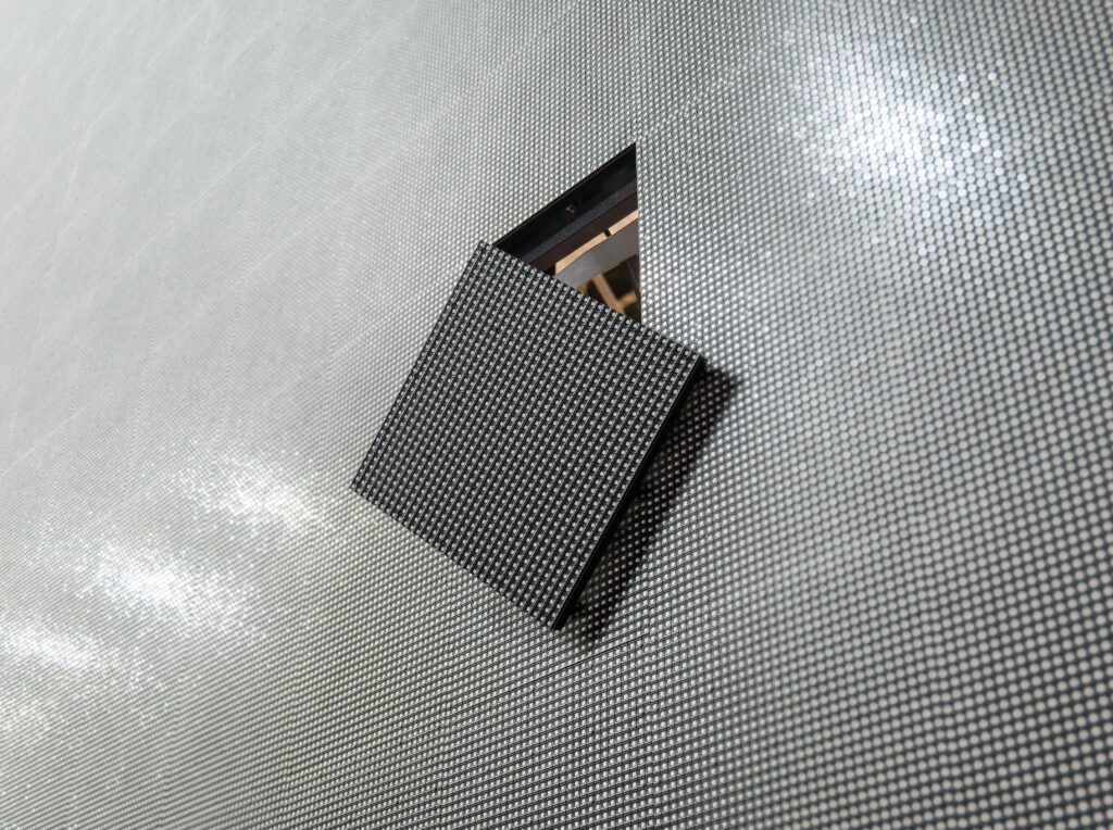 Close-up of a black LEGO plate with studs on a silver textured surface.