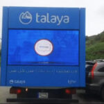 Talaya 3 Blue Talaya delivery truck with a large rear digital screen displaying content, parked in an outdoor lot near other cars.