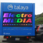 Talaya electro Blue Talaya billboard truck advertising Electro Media with rainbow text and Arabic script beneath, parked on a street edge.