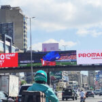 vivad jal eldib1 City street with large billboards overhead; red ad reads 'WIN 80 SMART TVs' while another shows 'PROMARCHÉ' in white and red, with traffic below.