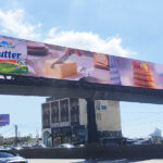 vivad jal eldib3 Overhead highway billboard advertising Plein Soleil Butter with a knife cutting butter and pastries above heavy traffic, during the day.