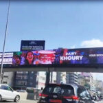vivad jal eldib4 Colorful advertising banners on a pedestrian bridge over a busy urban highway, with cars passing below.