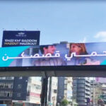 vivad jal eldib5 Blue advertising banner across a city overpass with Arabic text and partial images of people, urban buildings below.