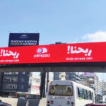 vivad jal eldib7 Red elevated billboard promoting Almaza anti-stress can over a busy city road.