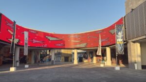 Large curved outdoor flexible LED screen display installed on a commercial building facade broadcasting a vibrant red digital advertisement at a themed entertainment destination.