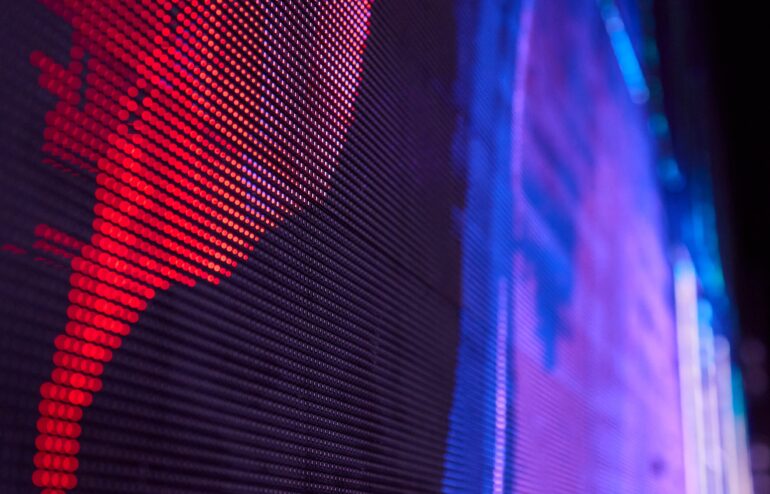 Close-up of a pixelated LED panel with red dots on the left and blue-purple glow on the right, creating a techy abstract pattern.